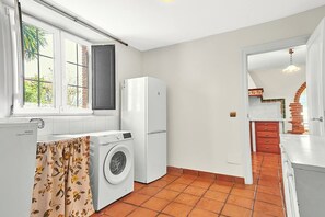 A compact kitchen with a washing machine, a refrigerator, and a window with curtains.