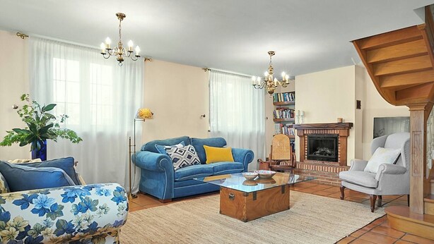 Een woonkamer met een bank, fauteuil, open haard en een trap.