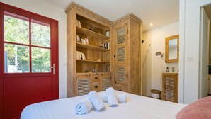 Une chambre à coucher avec un grand lit, une armoire en bois, une porte rouge et une fenêtre donnant sur des arbres.