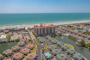 A coastal residential area with a large hotel featuring multiple floors and a distinctive orange roof, surrounded by smaller houses and a body of water. - 3BR- 5th floor- Lake & Golf View condo|Short walk to beach| Resort Access| (North Myrtle Beach)