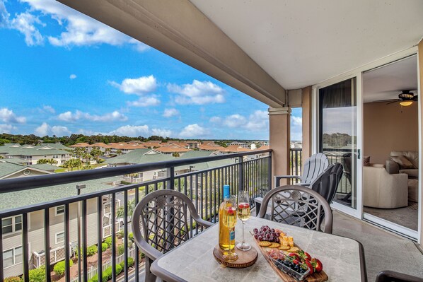 A balcony with a table set for two, featuring a bottle of wine, glasses, and a fruit platter. - 3BR- 5th floor- Lake & Golf View condo|Short walk to beach| Resort Access| (North Myrtle Beach)