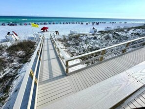 A wooden boardwalk leading to a beach with umbrellas and beach chairs.