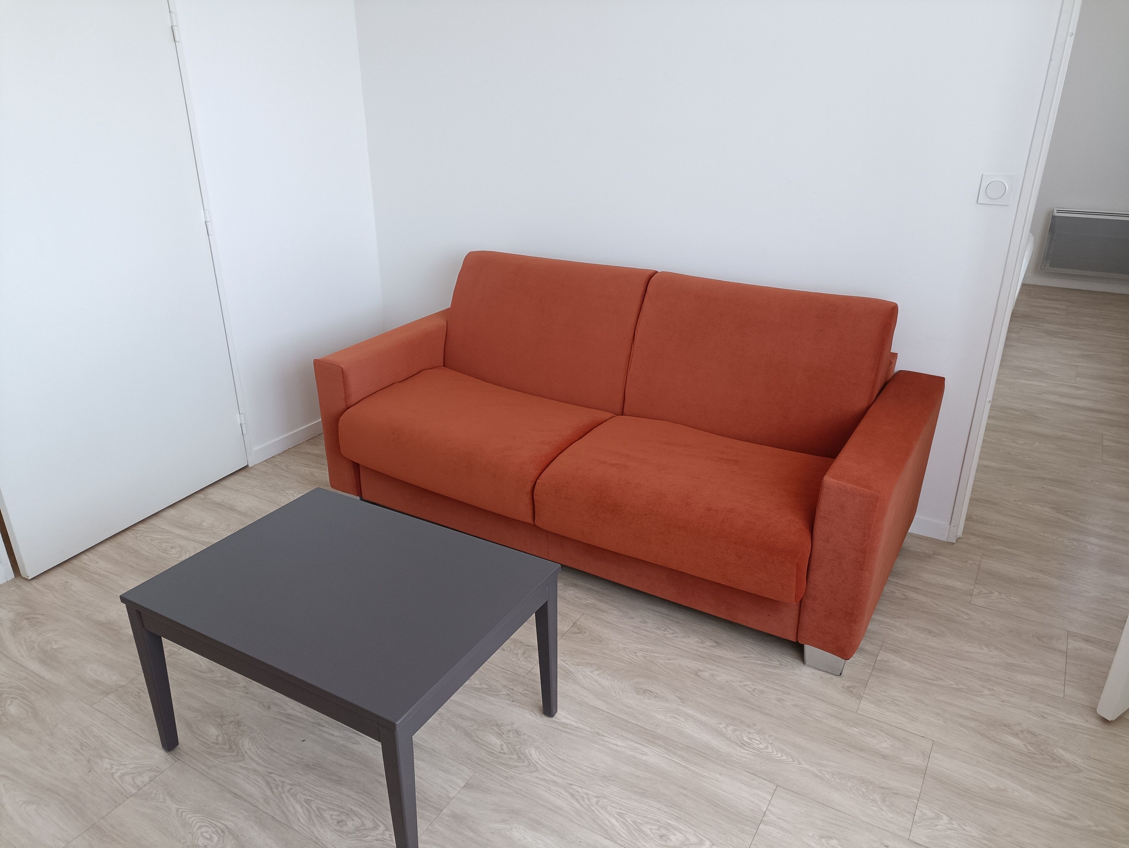 A room with a grey table and an orange sofa against a white wall.