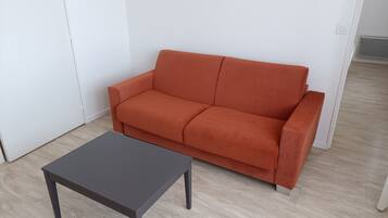 A room with a grey table and an orange sofa against a white wall.