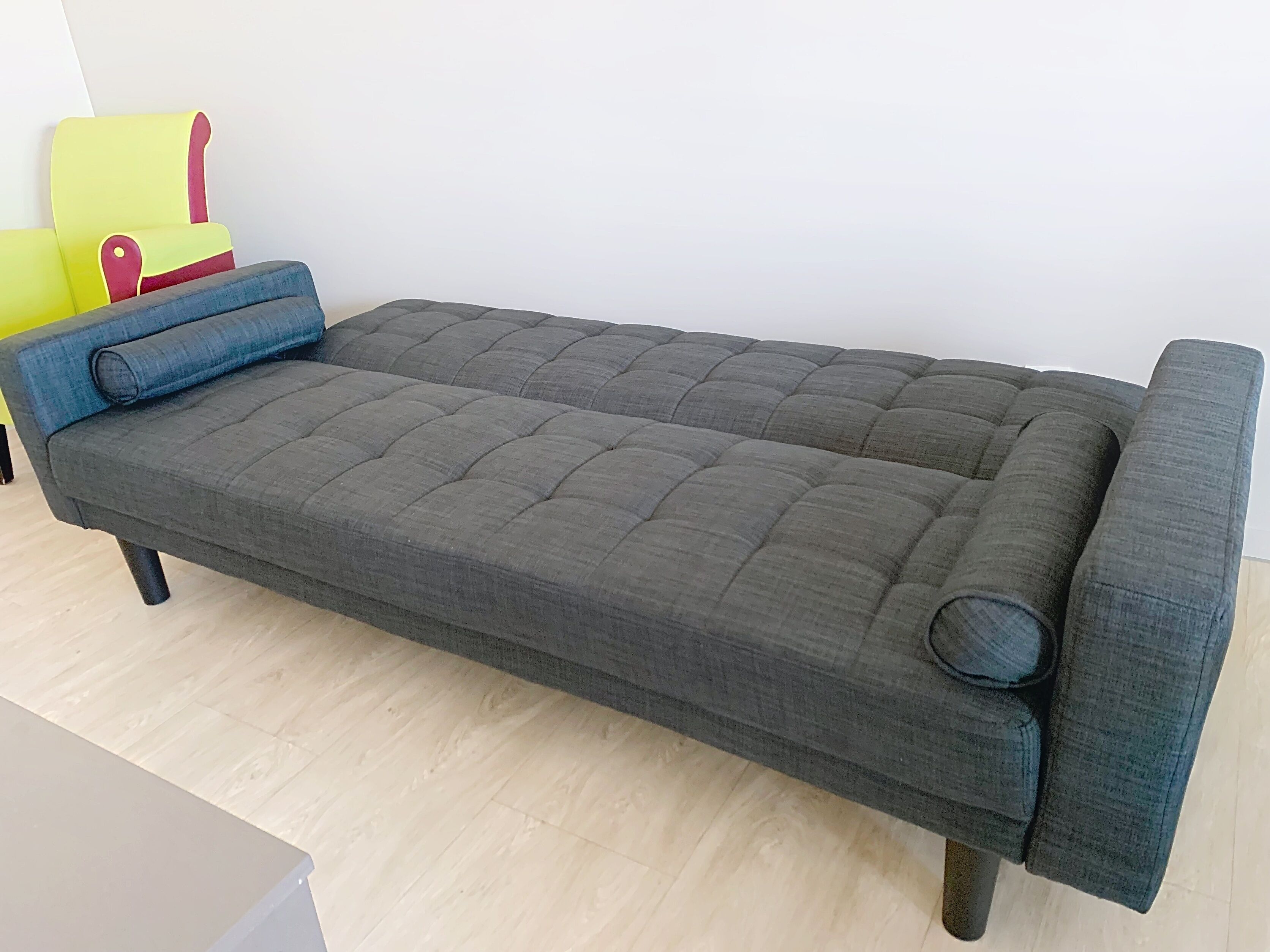 A single bed with a grey upholstered headboard and footboard, a blue pillow, and a matching blue cushion.