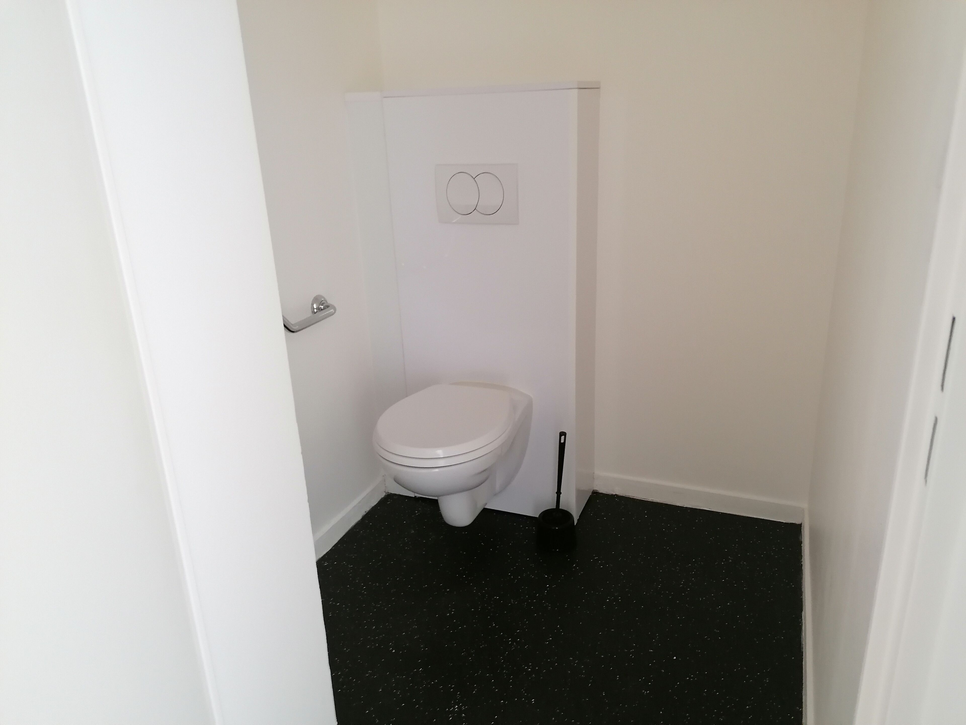 Un baño pequeño y blanco con inodoro, piso negro y puerta blanca.