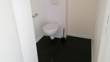 A small, white bathroom with a toilet, a black floor, and a white door.