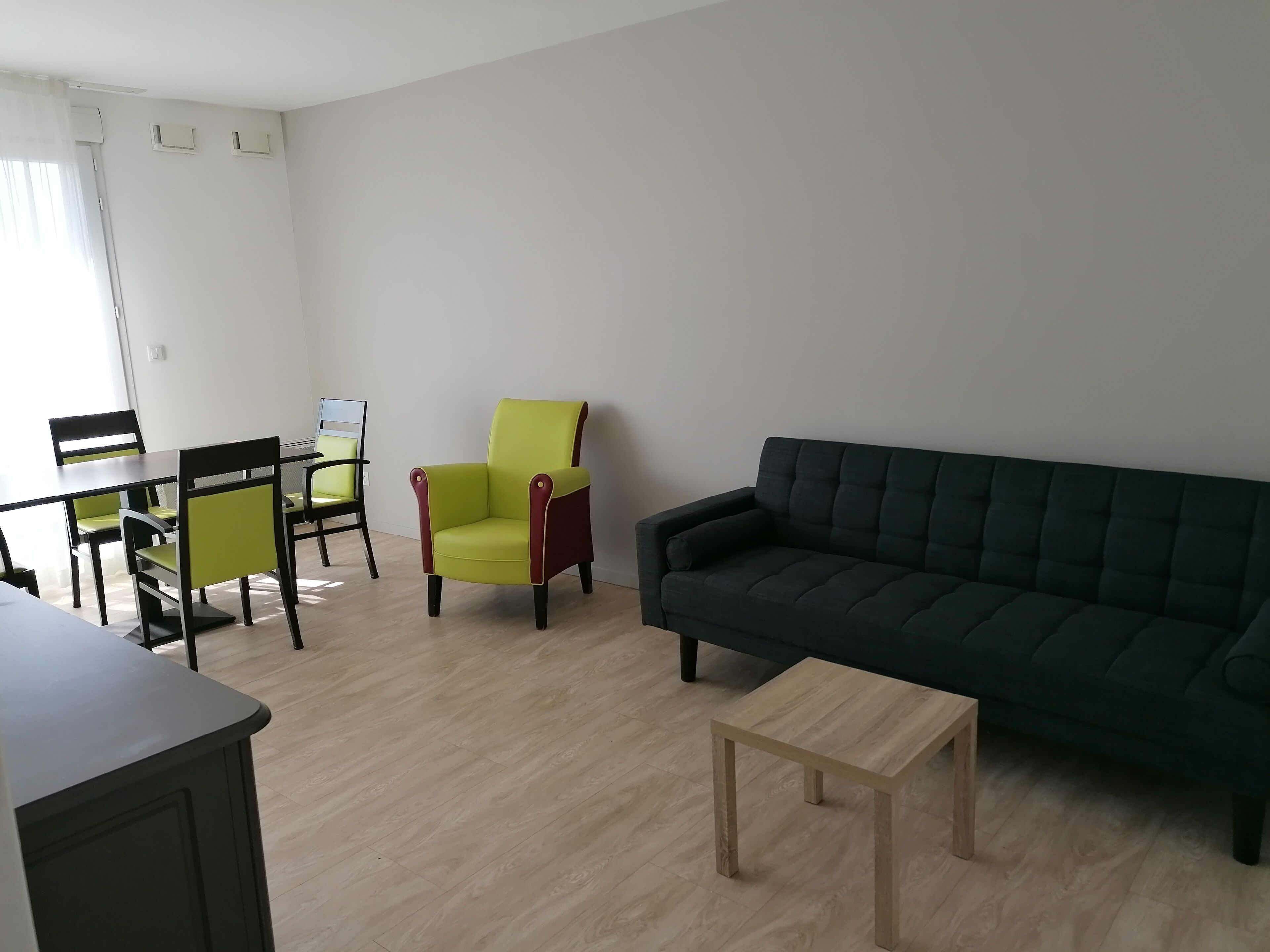 Una sala de estar con un sofá oscuro, una pequeña mesa de madera y un sillón verde.