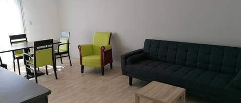 Una sala de estar con un sofá oscuro, una pequeña mesa de madera y un sillón verde.