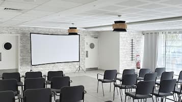 A conference room with rows of chairs, a whiteboard, and a projector screen.