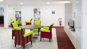 A modern library with a round table and striped chairs, surrounded by bookshelves. - Terres de France - Appart'Hôtel Rouen Flaubert (Rouen)