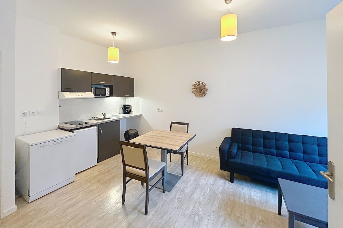 A compact kitchen with a dining area and a blue sofa.