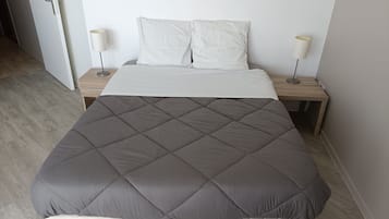 A bed with a grey quilt, white pillows, and two bedside lamps.