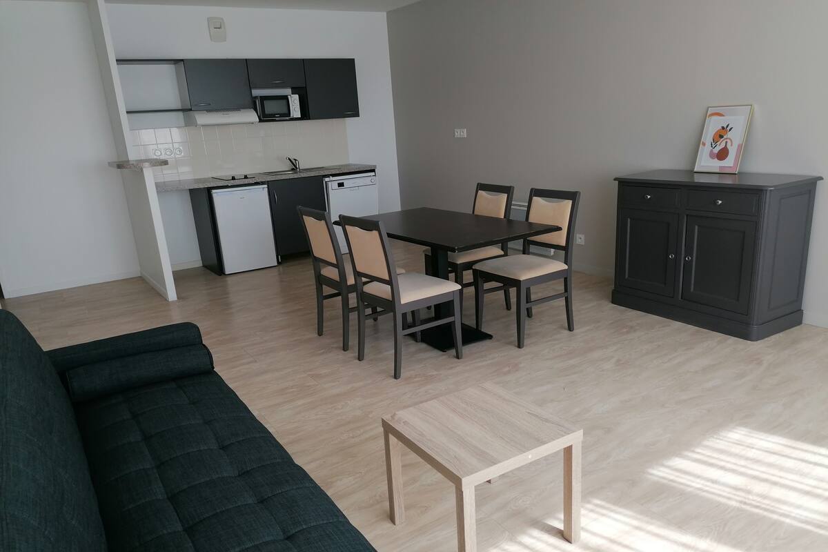 A modern living room with a dark green sofa, a wooden coffee table, and a dining area with a dark wooden table and beige chairs.