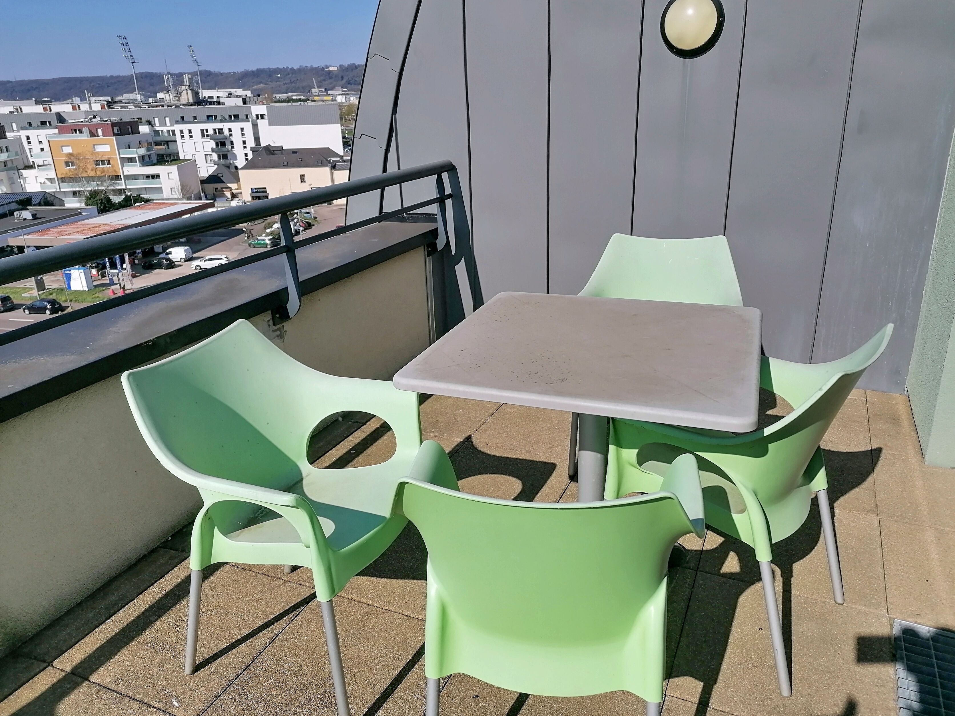 A balcony with a table and two chairs, a railing, and a view of buildings in the background.