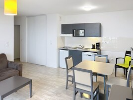 Cocina compacta equipada con microondas, cafetera y lavavajillas. Hay una mesa de comedor con sillas y un sofá en la zona de estar.