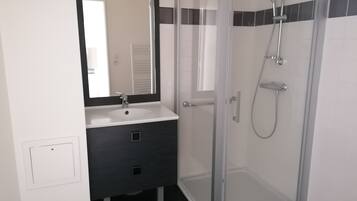 A bathroom with a glass shower enclosure, a white sink, and a dark vanity.