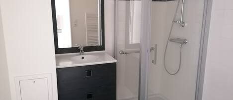 Un baño con cabina de ducha de vidrio, un lavabo blanco y un mueble de tocador oscuro.