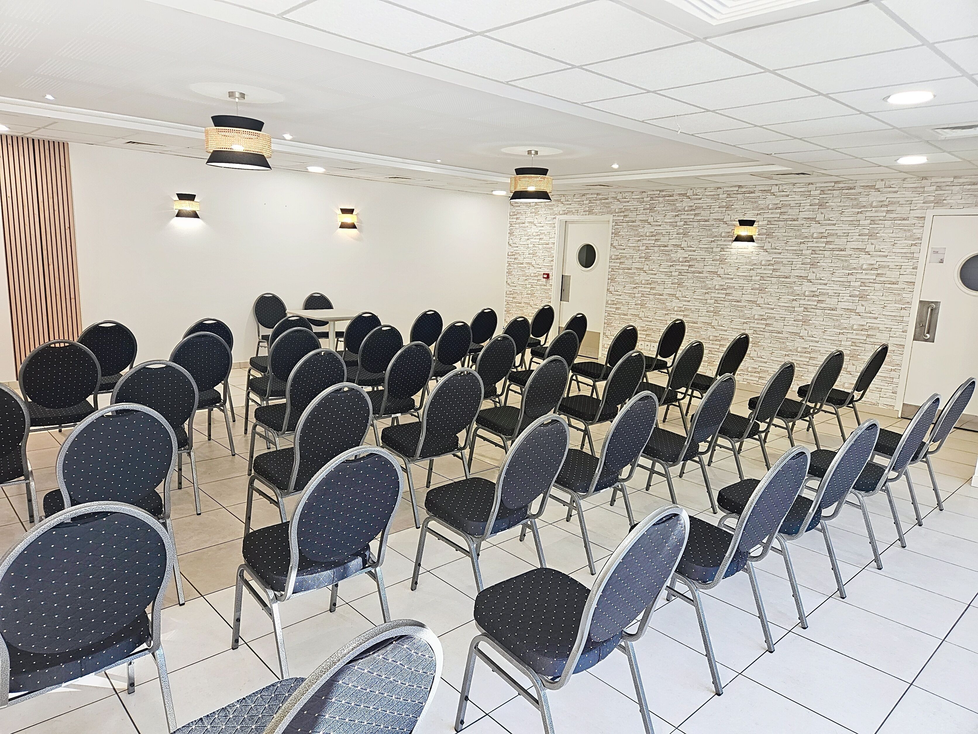 Une salle de conférence avec des rangées de chaises, une table blanche et un mur en pierre.