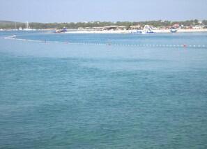 Vista sulla costa con acque calme, una spiaggia sabbiosa e alcune barche.