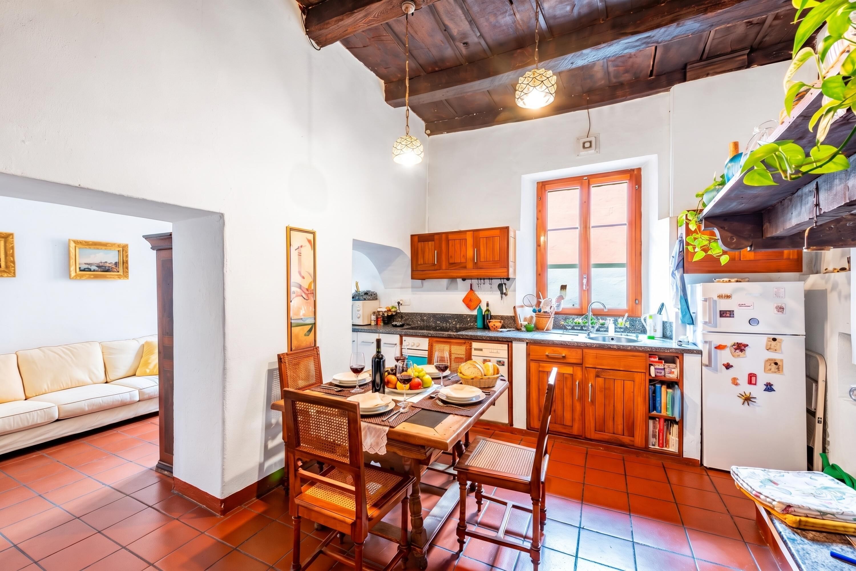 A cozy kitchen with wooden cabinets, a dining table set for two, and a refrigerator with magnets.