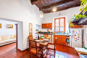 A cozy kitchen with wooden cabinets, a dining table set for two, and a refrigerator with magnets. - Antica Torre With Garden in Carona (Lugano)