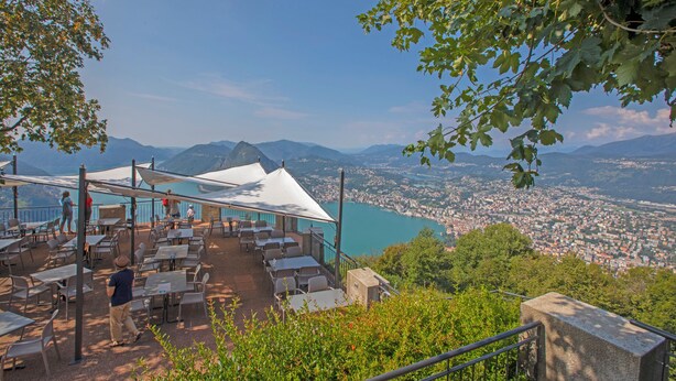 Une terrasse extérieure avec des tables et des chaises, offrant une vue sur un lac et sur le paysage urbain.