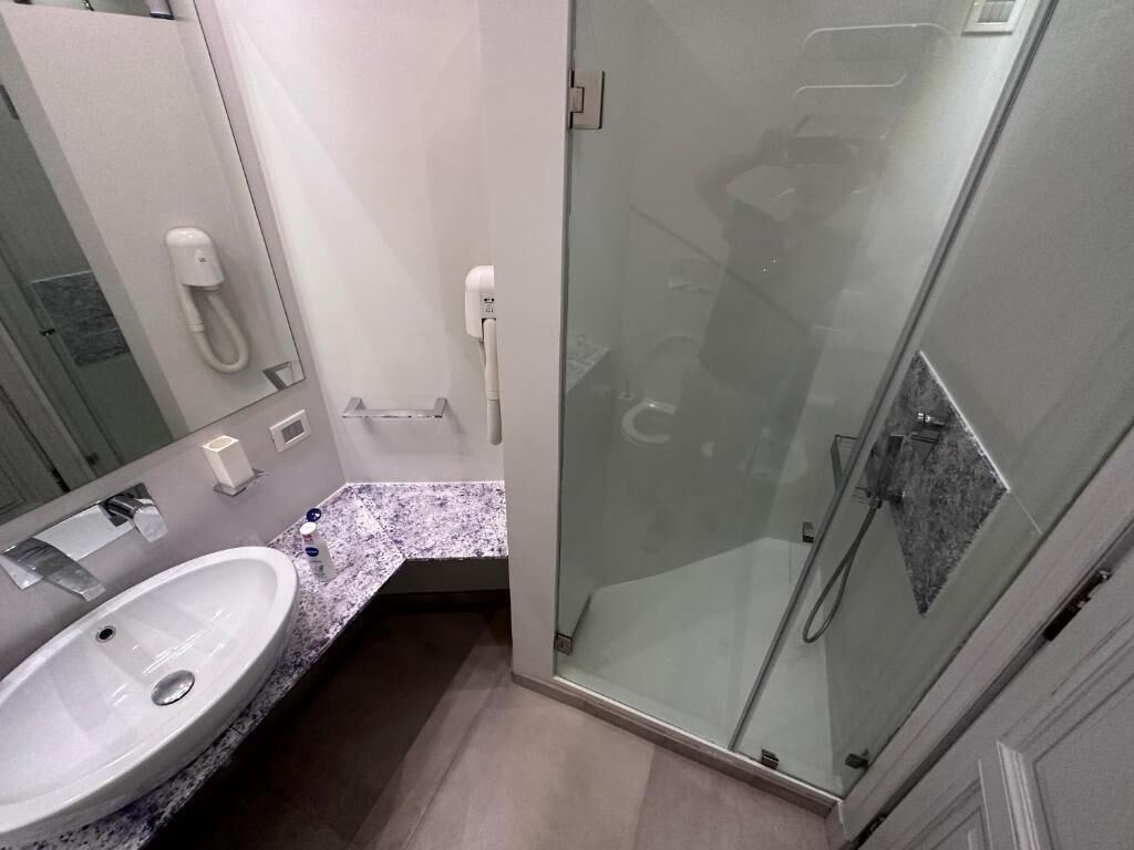 Ein modernes Badezimmer mit einer Duschkabine aus Glas, einem Waschbecken mit Marmorplatte und einer Toilette mit Papierhandtuchspender.