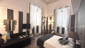 A hotel room with a large bed, a sofa, a TV, a mirror, and two windows with curtains. - Palazzo Franchi, noble and elegant mansion a few steps from the Pantheon (Roma)