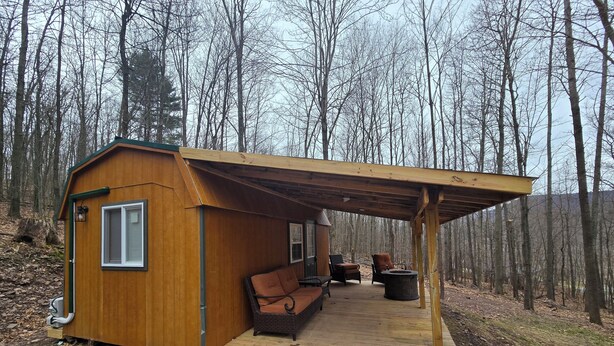 Une petite cabane en bois avec un porche couvert, deux chaises et un foyer.