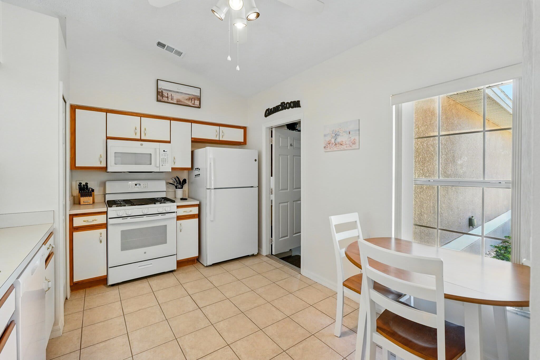 A kitchen with white appliances, a dining table with chairs, and a door labeled 'GameRoom'.
