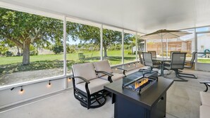 Un patio amplio con mobiliario exterior, una chimenea y ventanas grandes con vistas al jardín.