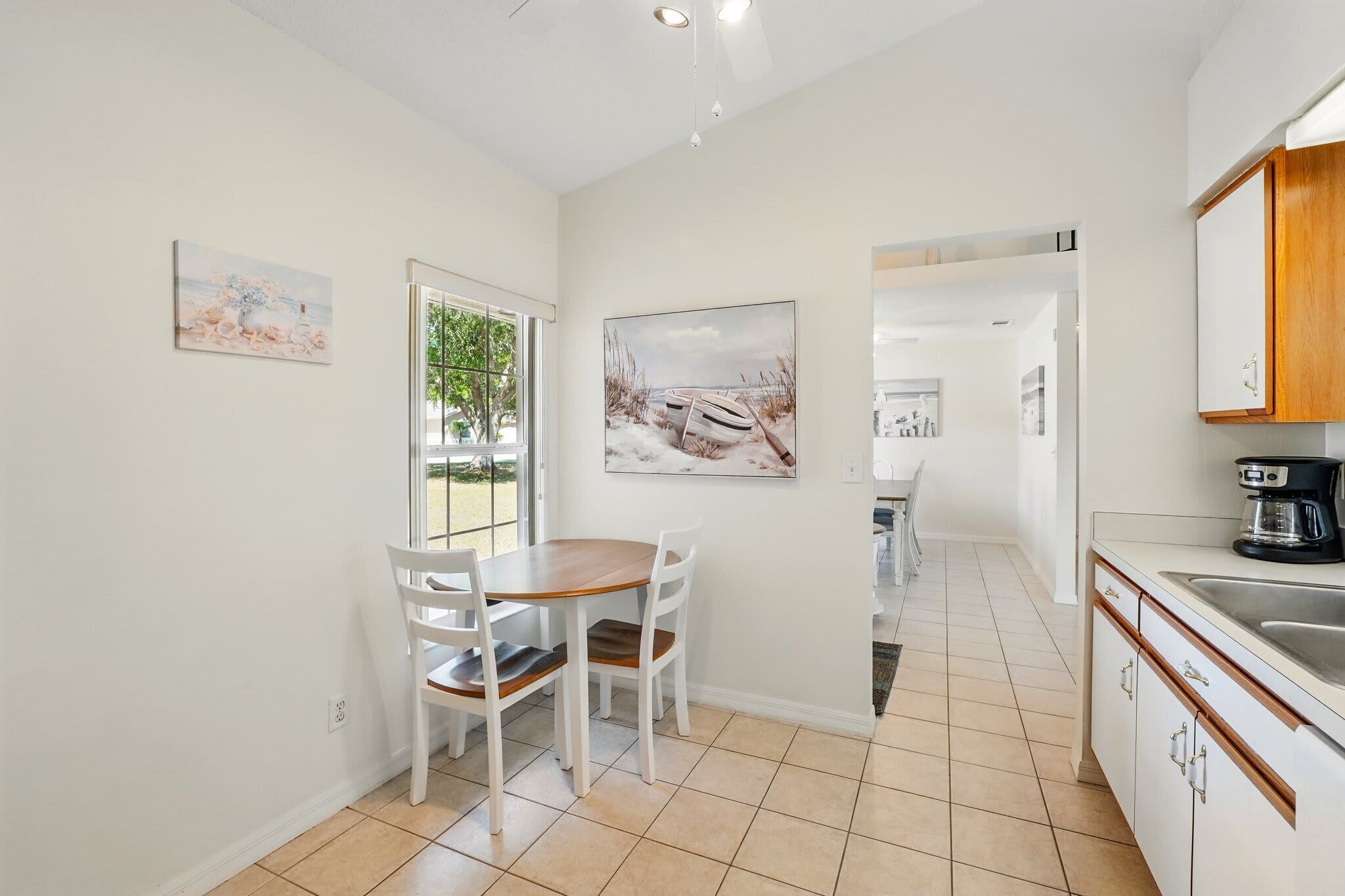 A modern kitchen with white cabinetry, a dining area with a wooden table and chairs, and artwork on the walls.