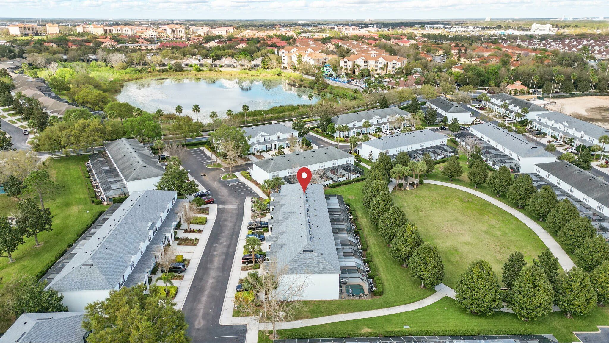 An aerial view of a residential area with multiple buildings, a central pond, and a red location marker.
