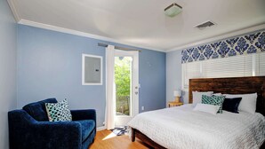 Un dormitorio con una cama, un sillón azul y una puerta que da a un balcón.