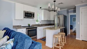 Una cocina moderna con armarios blancos, electrodomésticos de acero inoxidable y una isla central con taburetes.