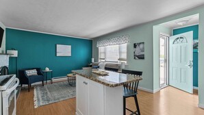 Une cuisine dotée d’un îlot central, un coin repas avec une table et des chaises, et un espace salon avec un canapé et une table basse.