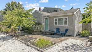 Une maison de plain-pied avec une porte verte, deux chaises bleues à l’extérieur et un petit jardin.