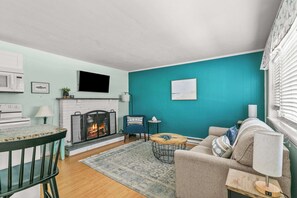 Un salon aux murs de couleur turquoise, avec une cheminée, un canapé, une table basse et un téléviseur fixé au mur.