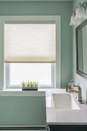 A bathroom with a window, a sink, a mirror, and a light fixture.