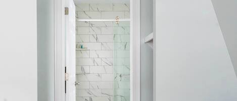 A room with a wooden floor, a blue chair, and a glass shower door with white tiles.