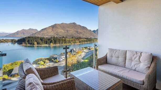 A balcony with wicker furniture, a view of a lake, mountains, and a clear sky.