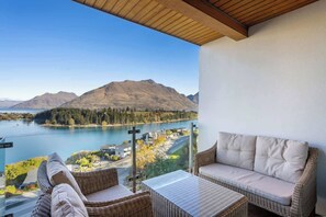 Un balcon agrémenté de meubles en osier, avec vue sur un lac, des montagnes et un ciel dégagé.