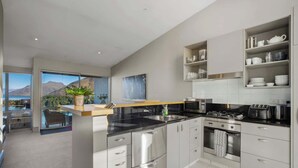 A modern kitchen with stainless steel appliances, a dining area with a view, and a balcony with a mountain backdrop.