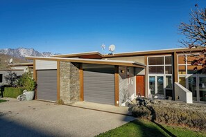 Une maison moderne avec un garage, un pilier en pierre et une antenne parabolique.