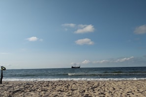 A beach with a boat in the distance and a clear sky.