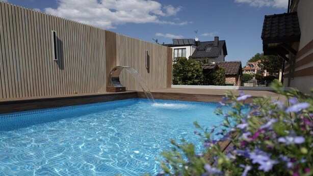 En swimmingpool med en træterrasse og et hus i baggrunden.