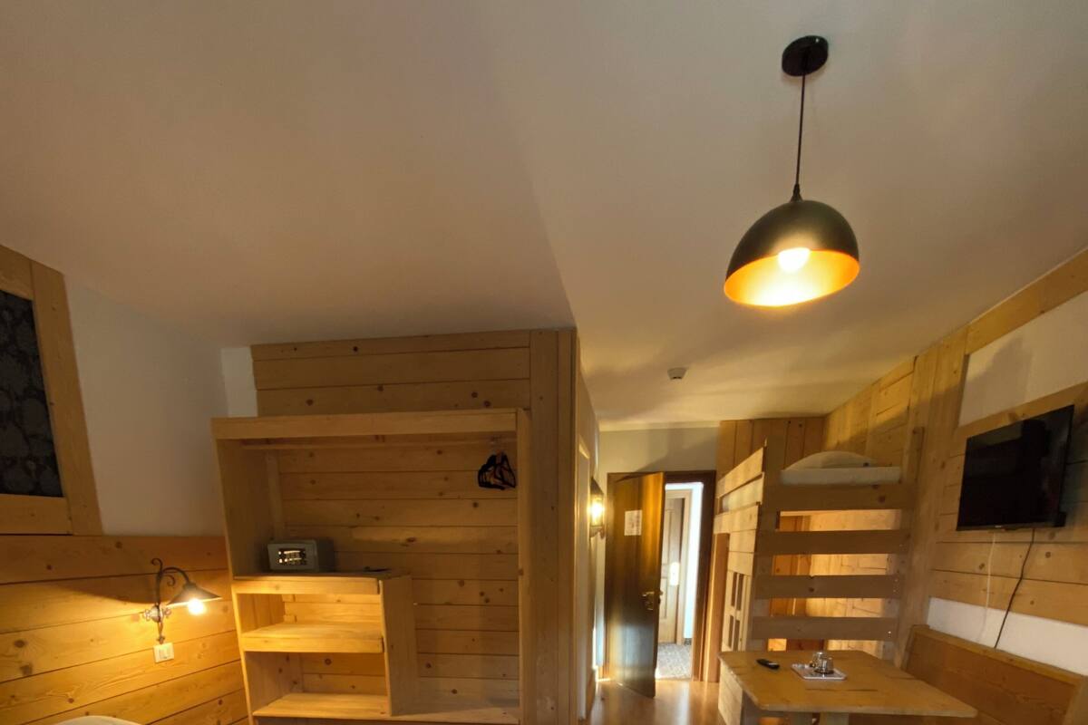 A wooden cabin-style room with two beds, a desk, and a TV mounted on the wall.