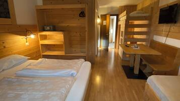 A wooden cabin-style room with two beds, a desk, and a TV mounted on the wall.