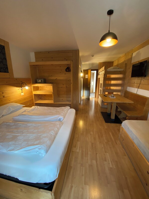 A wooden cabin-style room with two beds, a desk, and a TV mounted on the wall. - Hotel Almhof (San Candido)